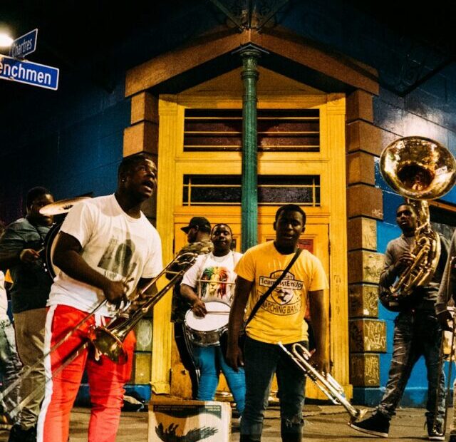 people holding musical instruments while standing on street during nighttime