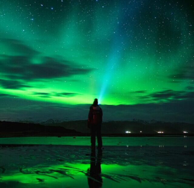 person standing on seashore under green sky with stars during night time