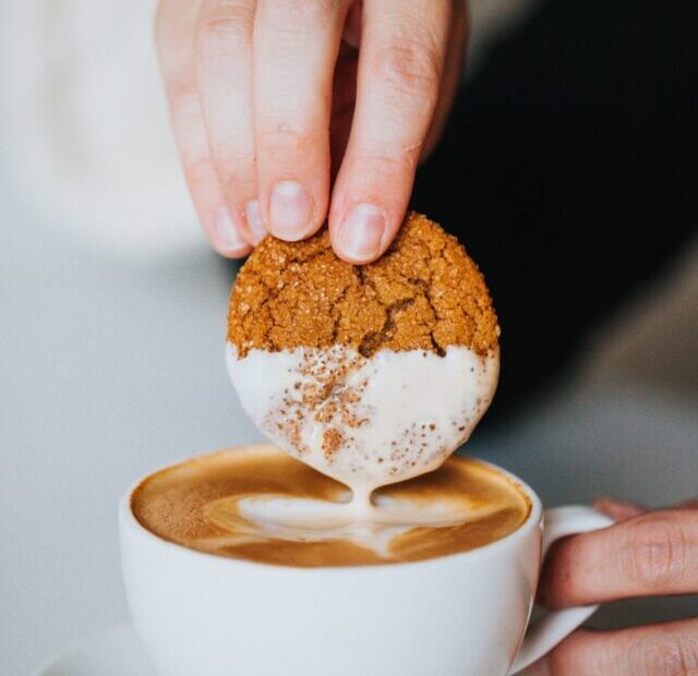 person holding white ceramic mug with brown and white liquid