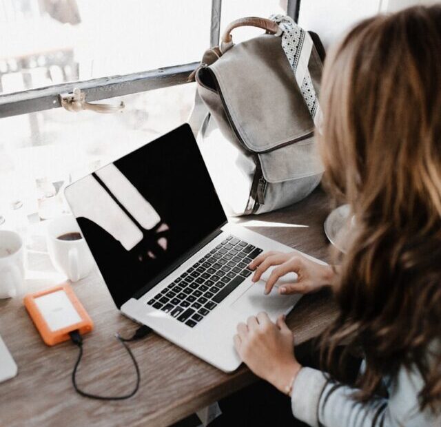 girl wearing grey long-sleeved shirt using MacBook Pro on brown wooden table